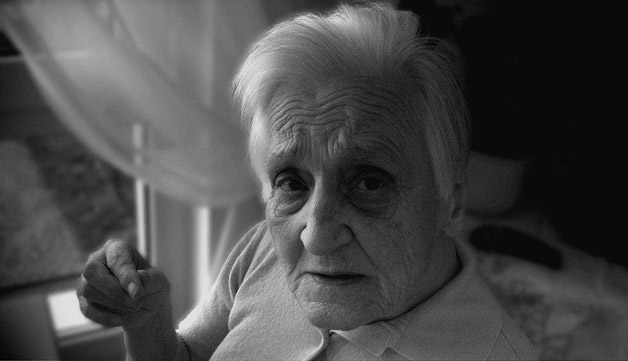 Elderly woman, with a scared look, stands by the window at her home